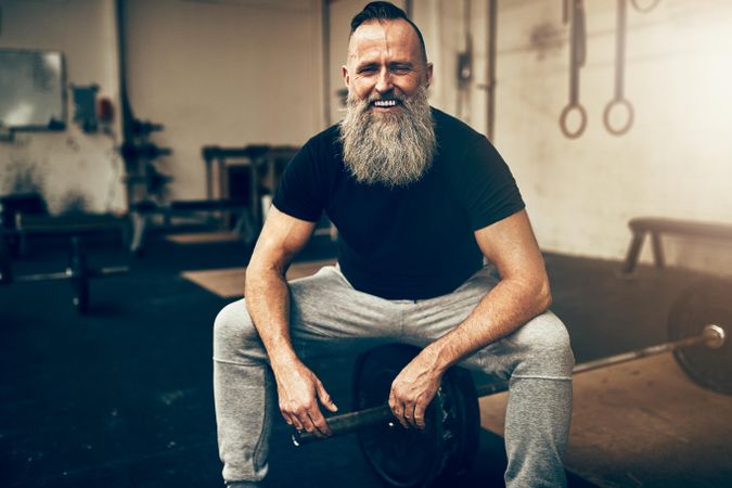 Smiling man with big grey beard sitting in weightlifting gym