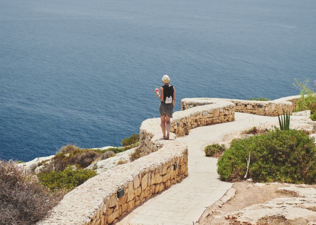 Back of person balancing on stone wall above the Mediterranean Sea