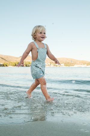 Happy little toddler splashing and promenading in sea under clou