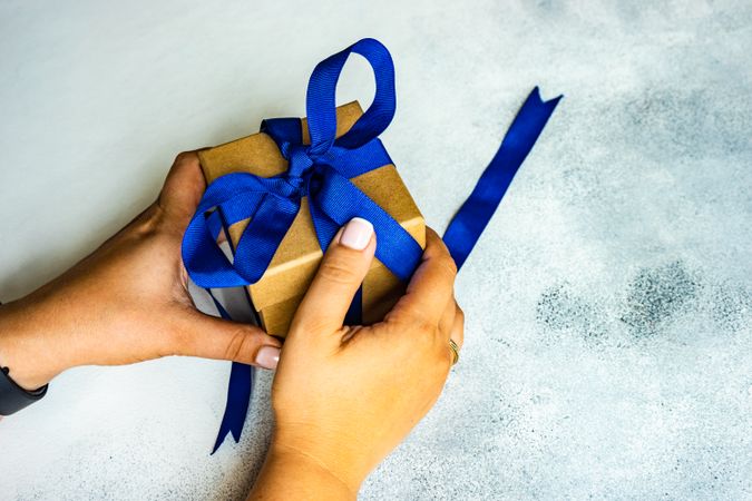 Hands holding gift wrapped in blue ribbon