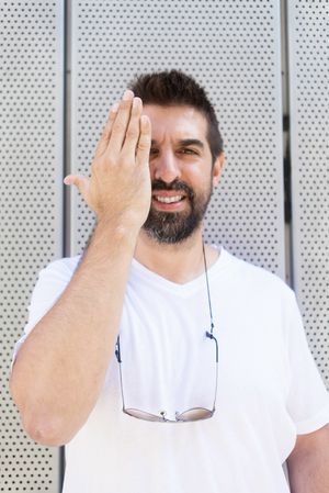 Latino man standing outside holding hand up to eye