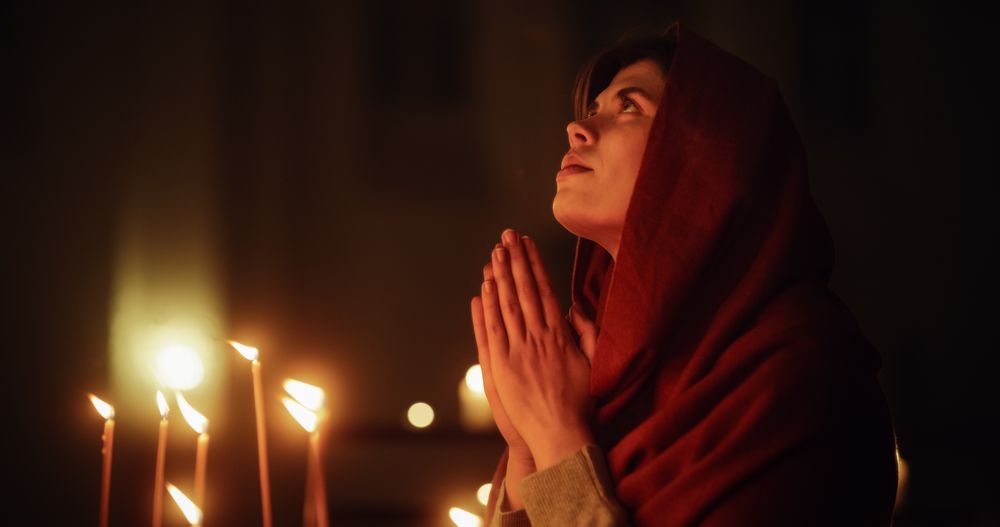 Christian Woman with Head Scarf Getting on her Knees and Praying Near the Candles in a Church.