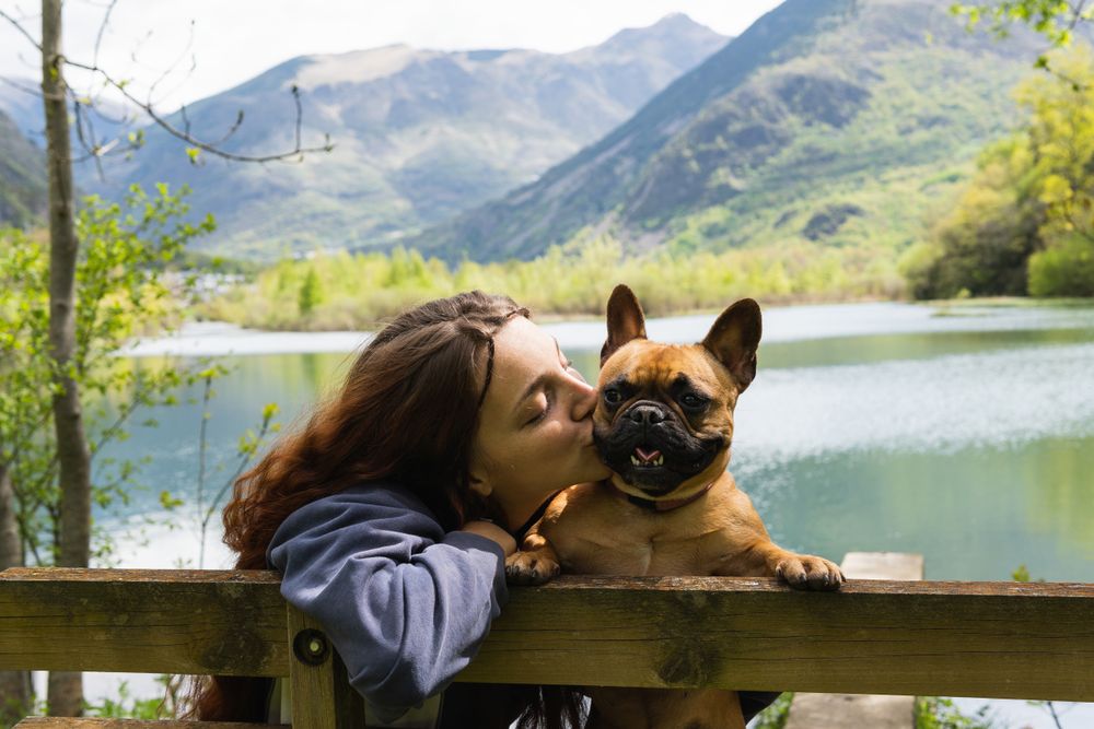 Female traveler kissing dog near lake in mountains
