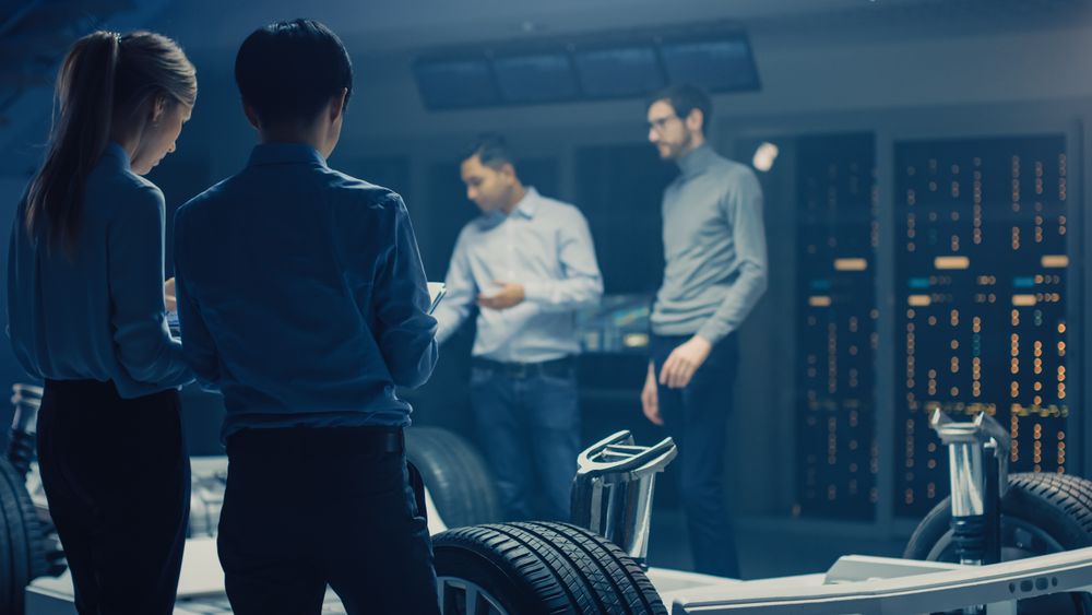 Automobile Engineers Discussing and Designing Electric Car Chassis Platform, Using Tablet Computers with 3D CAD Software
