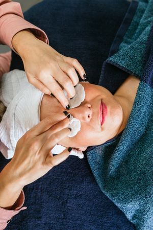 Crop beautician applying toner on face of female client in beauty salon