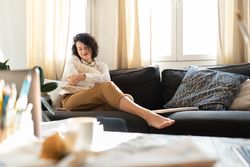 Woman with pillow on sofa near table with brushes and laptop