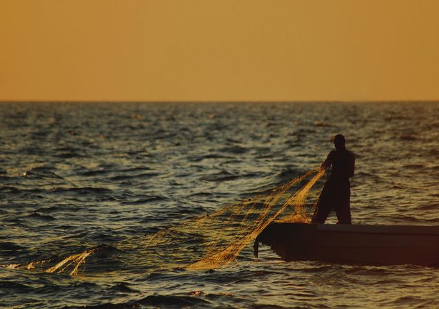 Silhouette of man in a boat fishing with a net at sunset