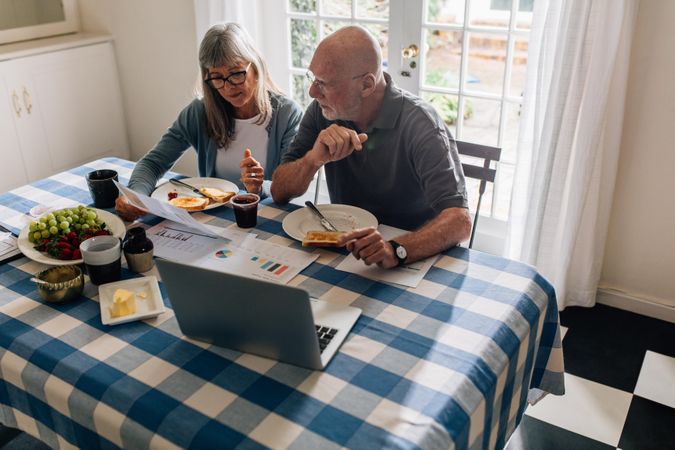 Man and woman having breakfast together at home with a laptop and papers on the table