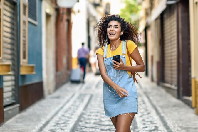 Arab woman listening to music with earphones and dancing in street