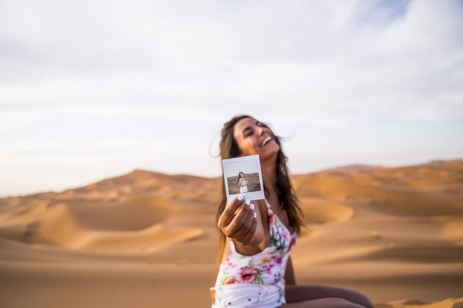 Happy woman showing instant photo in desert