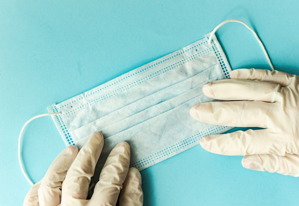 Covid-19 virus concept of hands in latex gloves holding facemask on blue surface