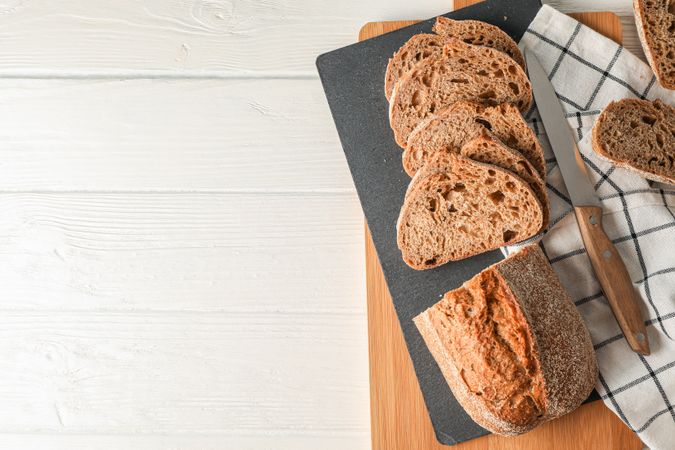 Composition with bread, knife, kitchen towel and cutting board on wooden background, top view and space for text