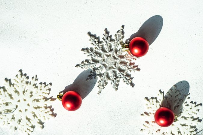 Top view of decorative snow flakes and red baubles with shadow