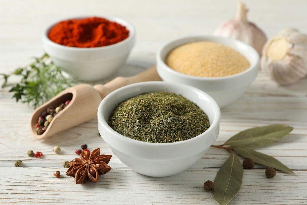 Side view of wooden scoop full of peppercorn with bowls of spice