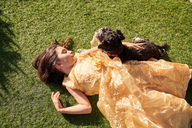 Happy girl in dress lying on green field with dog