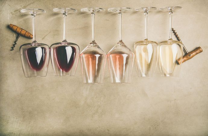 Glasses of wine laying on grey background with corkscrew, copy space