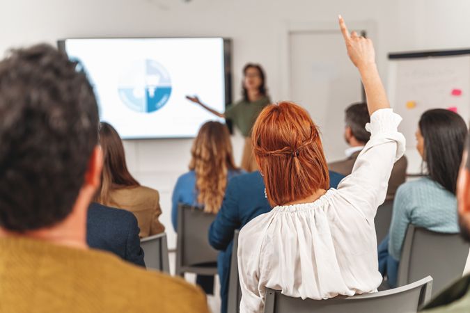 Businesswoman with red hair raising hand to ask question during a SWOT analysis presentation in large office room