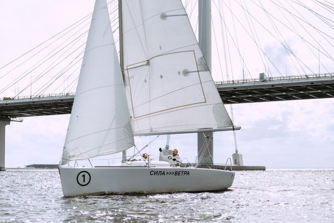 Two men on sailing boat near bridge