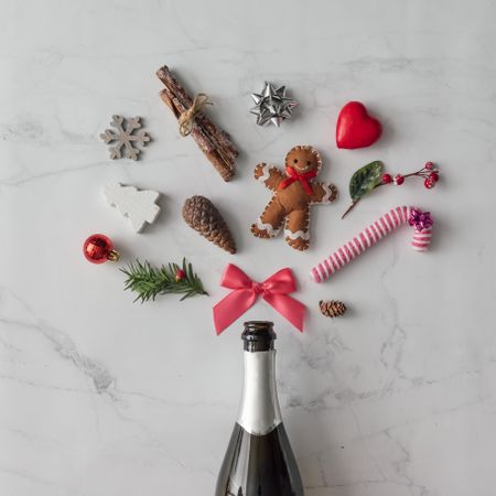 Champagne bottle with festive decorations; ribbons, candy cane, gingerbread, on marble background