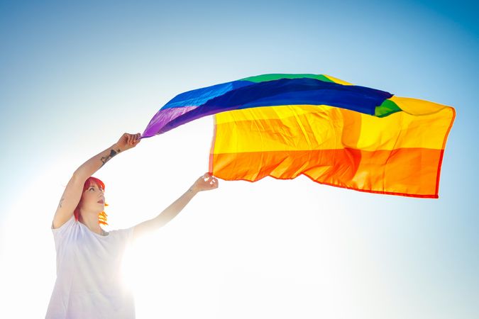 Young woman waving Pride flag under blue sky