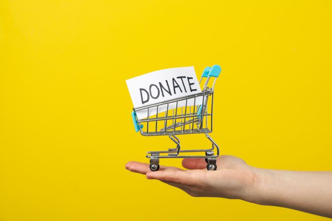 Female hand holds shop cart with text Donate on yellow background
