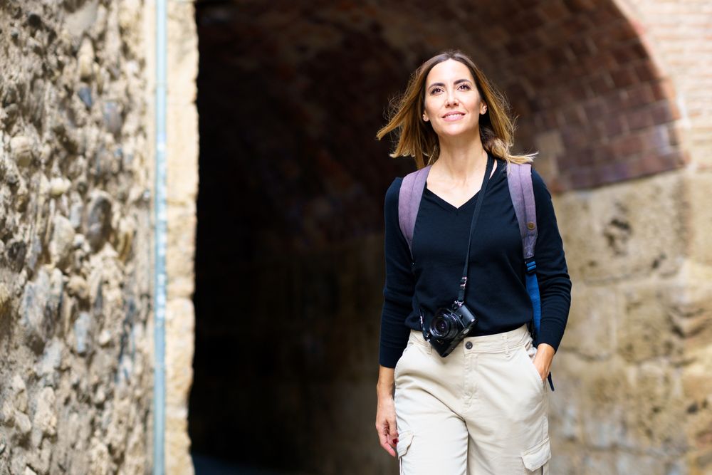 Smiling female with camera walking away from arched passage in old town