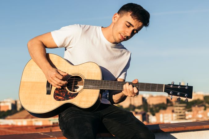 young man sitting playing acoustic guitar on a rooftop