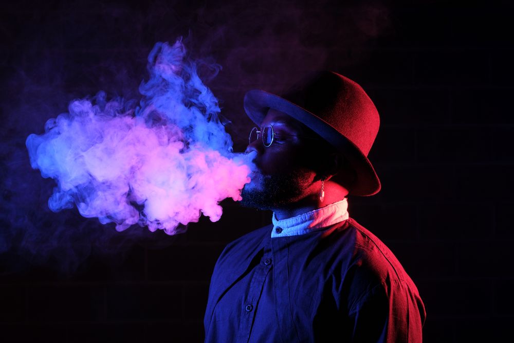 Young Black man with vape in dark room