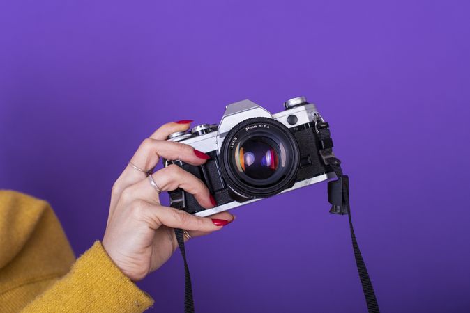 Close up of a female hand holding a film camera over a violet background.