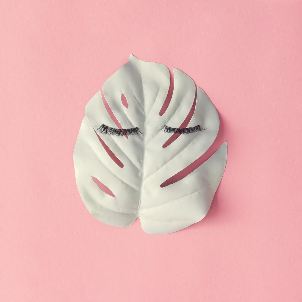 Face of false eyelashes on light leaf on pink background