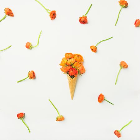Waffle cone with orange buttercup flowers on a light background with decorative flowers arranged
