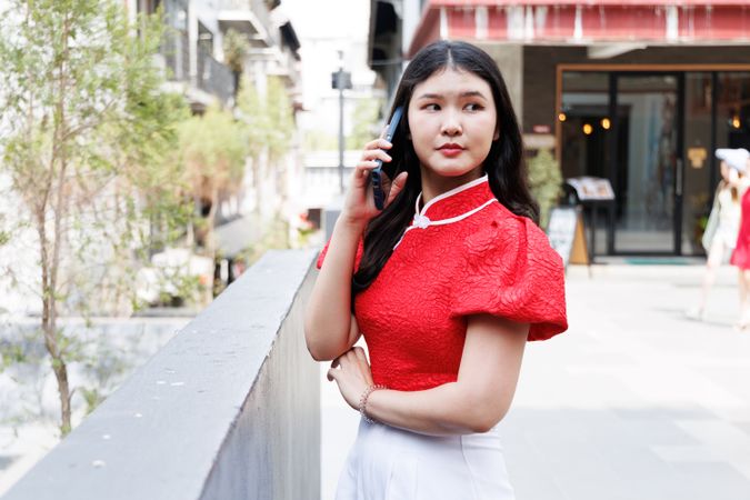 Asian person talking on mobile phone standing in the city in red shirt
