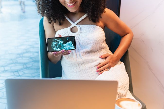 Anonymous Black pregnant woman showing baby ultrasound picture to laptop