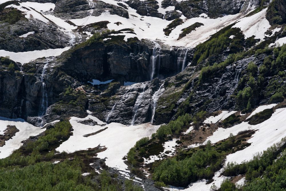 Snowy mountains with cascading waterfalls and green vegetation