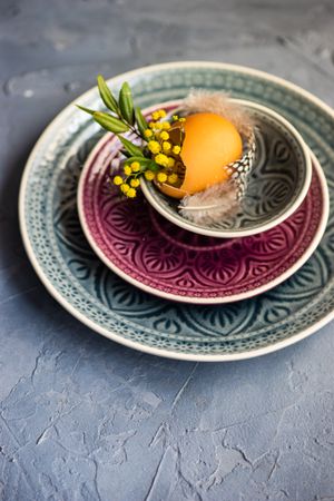 Easter table setting with egg, feather and foliage on patterned plate