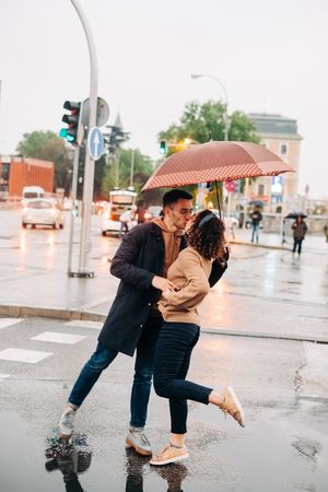 Happy couple with umbrella hugging on wet street