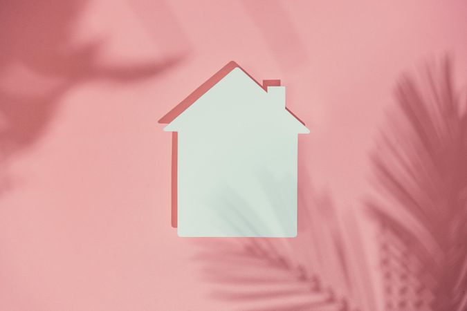 Paper house on pink background with palm leaf shadows