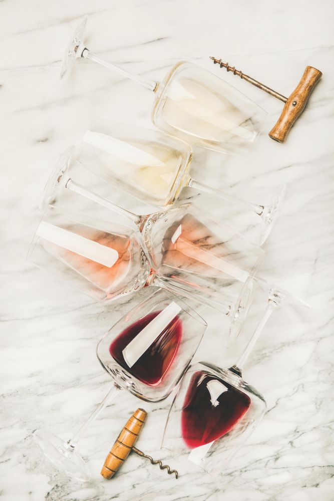 Glasses of wine laying on marble background with corkscrew