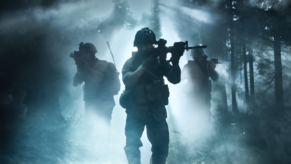 Silhouette of the Fully Equipped Soldier Moving Through Smokey Forest with Rifle Ready To Shoot.