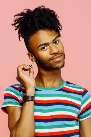 Smiling young man with earrings, happy sign on his striped shirt and hand up