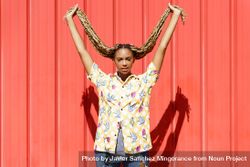 Woman holding up her braids in front of a red wall 4j9gz5