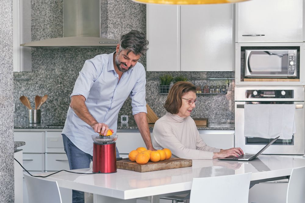 Smiling adult son making orange juice near mature mother in kit