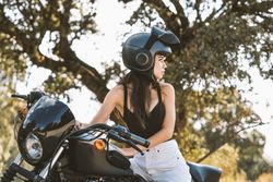 Attentive woman in helmet sitting on parked motorcycle at rural area