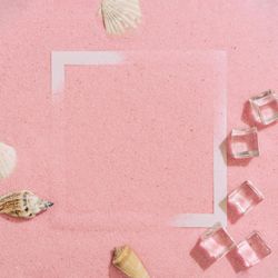 Pink sand with paper square outline and ice cubes, palm leaf and sea shells