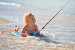 Excited toddler on surfboard on sandy beach