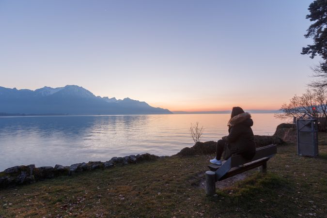 woman on wooden seat in lake and mountains
