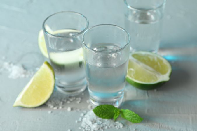 Tequila shots, salt, lime slices and mint on cement background