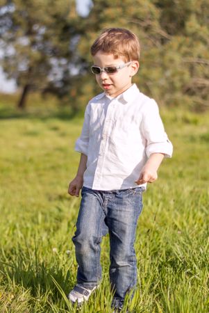 Happy cute kid walking by the grass of sunny field