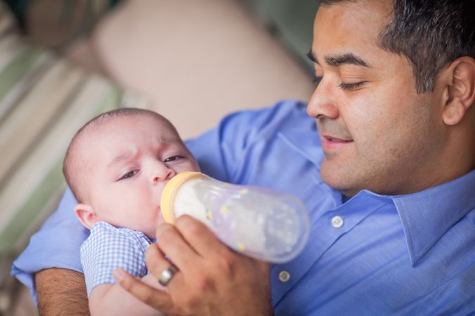 Happy Hispanic Father Bottle Feeding His Very Content Son.