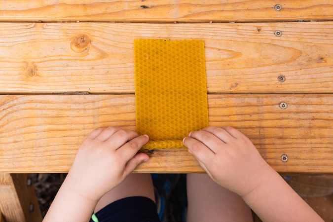 Crop kid creating beeswax candle at table